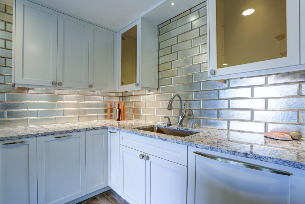 Modern white kitchen design with silver backsplash, white shaker cabinets and gray quartzite countertops.